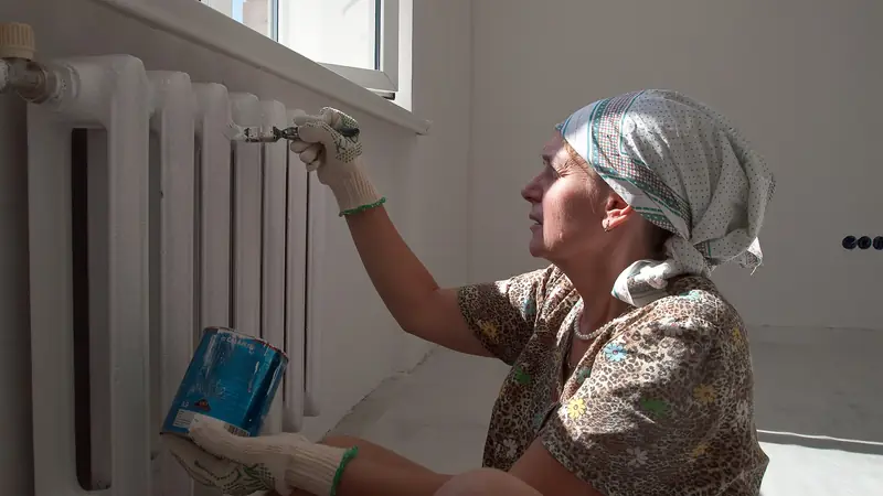 Maler Offerte Solothurn: Handwerkerin lackiert einen Heizkörper unter dem Fenster mit weissem Lack