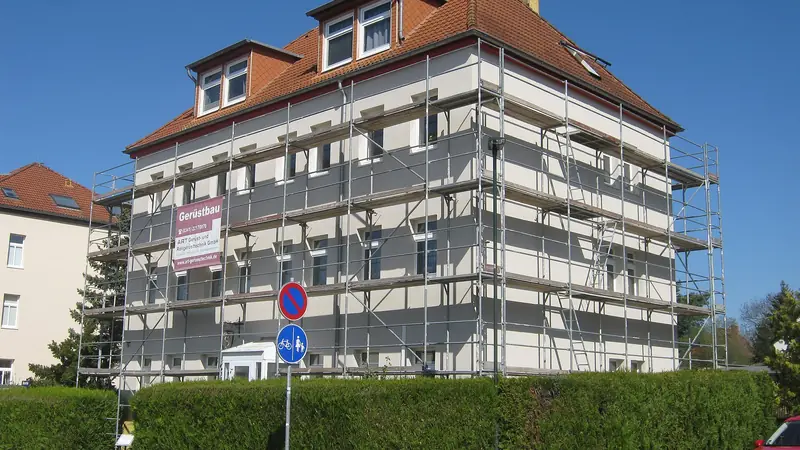 Malerarbeiten Solothurn: Eingerüstetes Mehrfamilienhaus mit Walmdach während der Fassadenrenovation