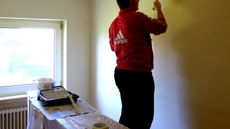 Mann streicht in einer Wohnung eine Wand neben dem Fenster weiss